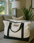 White canvas tote with black handles, vinyl bottom, and leather Colorado Tent logo