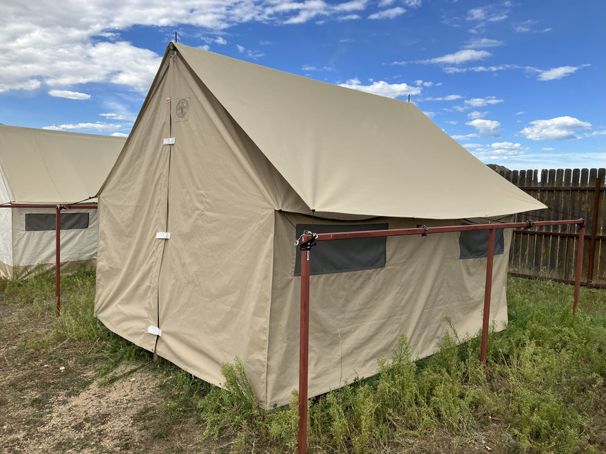 Tan canvas wall tent with a fly, pitched on a steel frame beside a second tent under blue sky.
