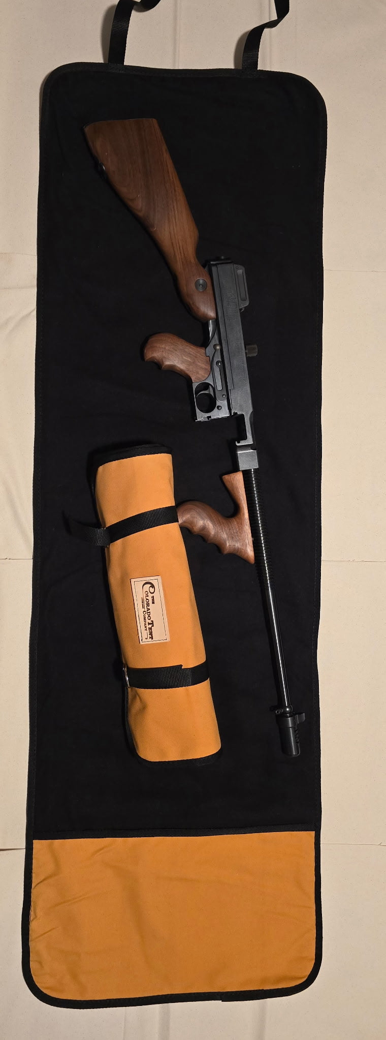 Black cleaning mat with a rolled tan tool pouch and a wood-stocked shotgun laid across it.