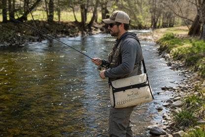 Fly angler on a wooded river wearing the ArctiCreeL creel on a shoulder strap