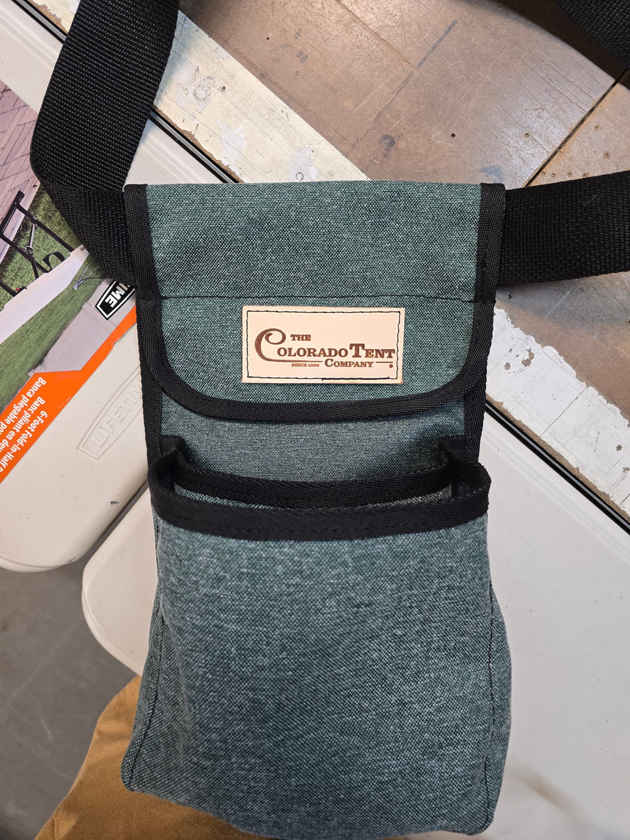 Green canvas shell bag with a flap, a Colorado Tent Company label, and a black shoulder strap.
