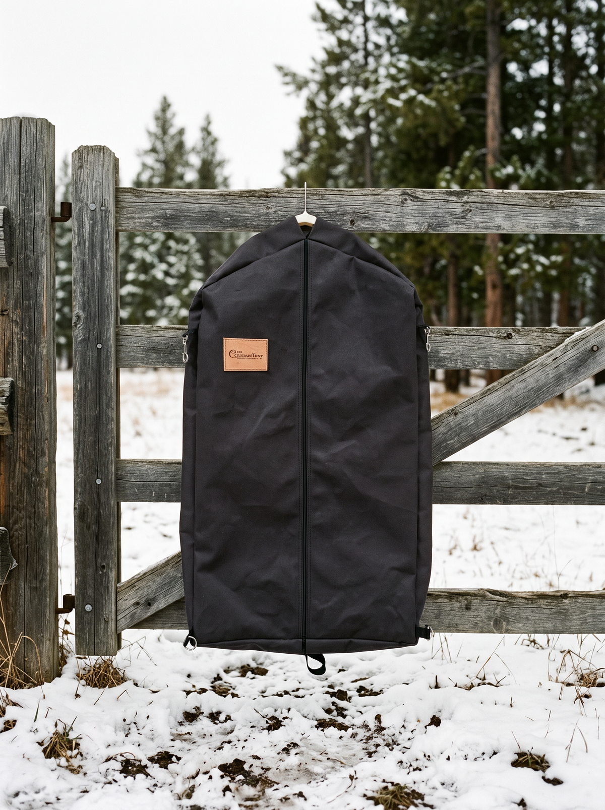 Black waxed canvas Colorado Garment Bag hanging on a wood fence in the snow