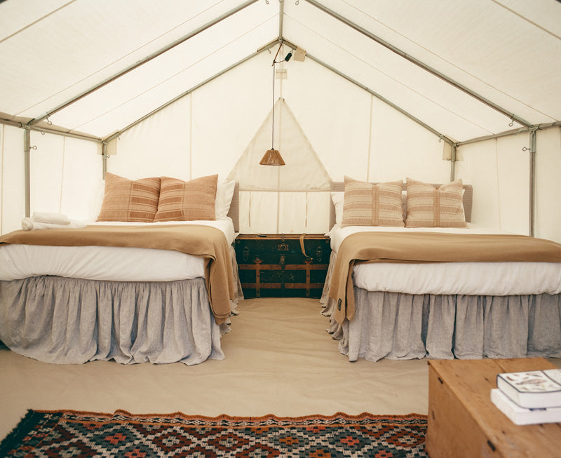 Wall tent interior set up for glamping with two made beds, a vintage trunk, and a hanging lantern.