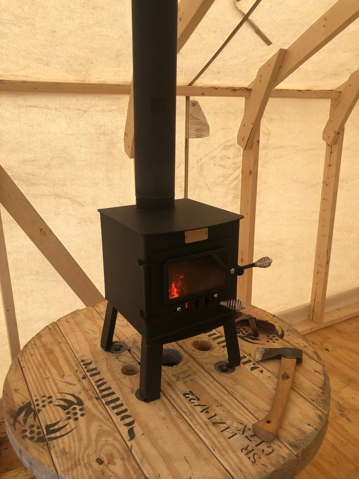 Mini Woodsman Wood Stove by North Woods Fabrication, burning in a canvas wall tent, stove pipe through the roof