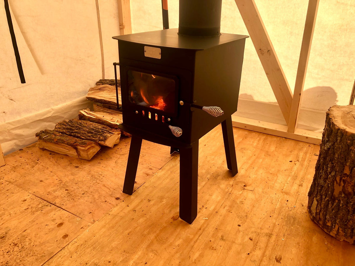 Woodsman Wood Stove by North Woods Fabrication, burning in a canvas wall tent