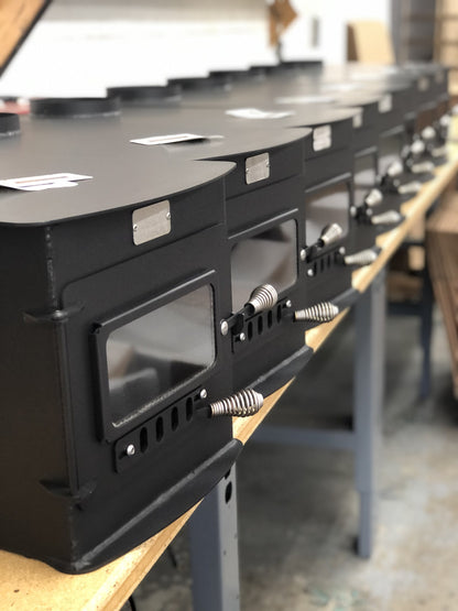 Woodsman XL Wood Stove by North Woods Fabrication, a row of Woodsman XL stoves in the North Woods shop