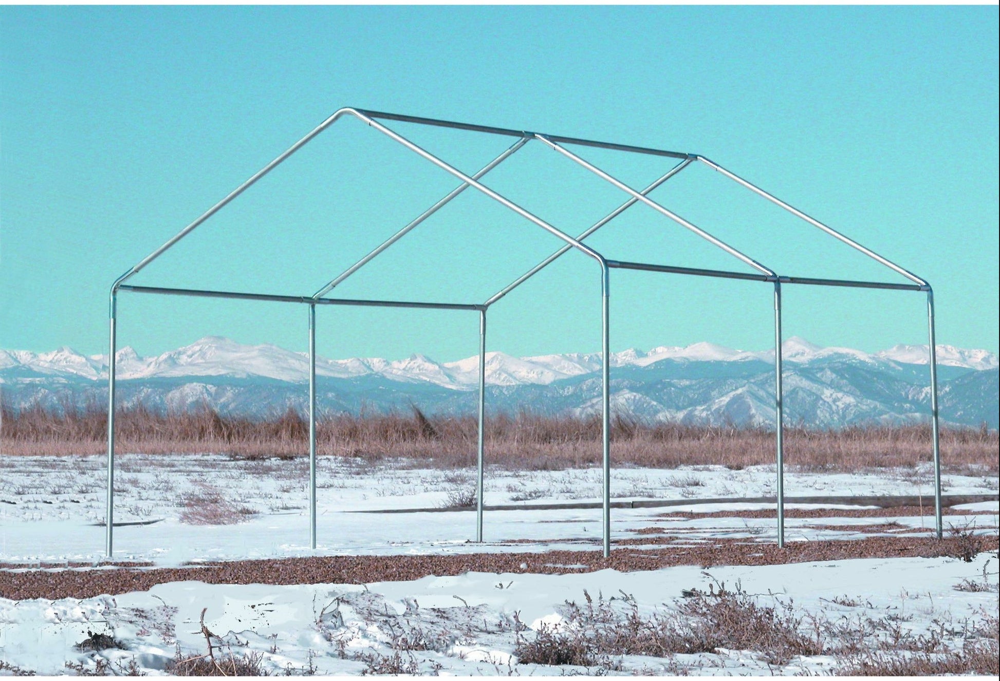 Bare galvanized steel tent frame standing in a snowy field with a mountain range behind it.