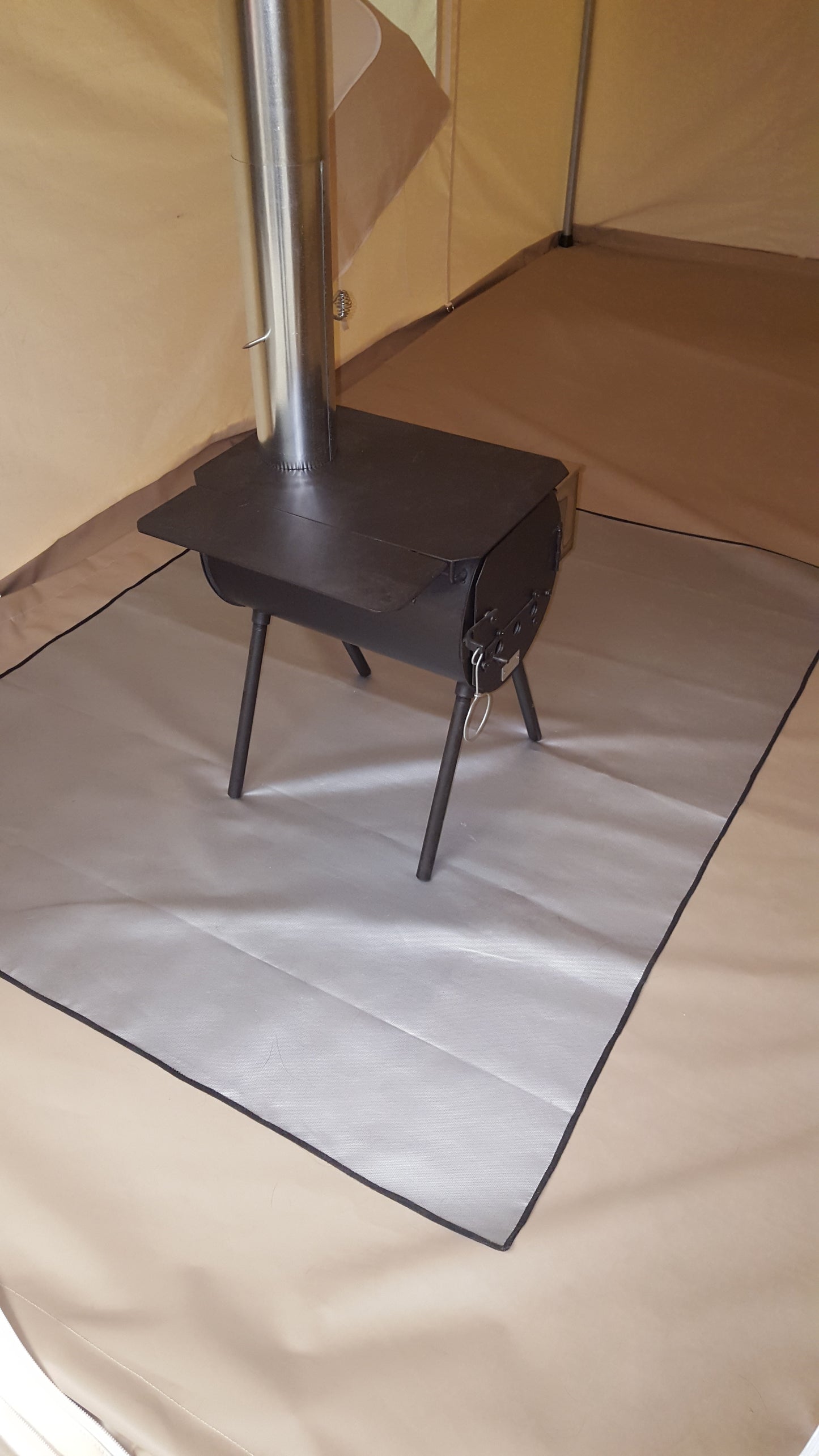 Gray protective mat under a small wood stove and stovepipe inside a canvas tent.