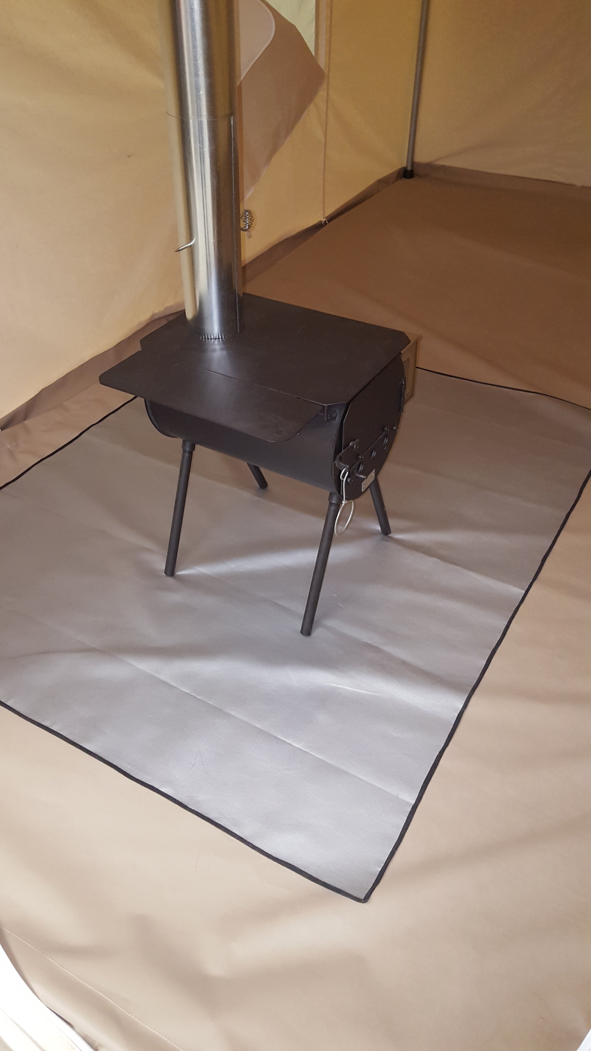 Gray protective mat under a small wood stove and stovepipe inside a canvas tent.