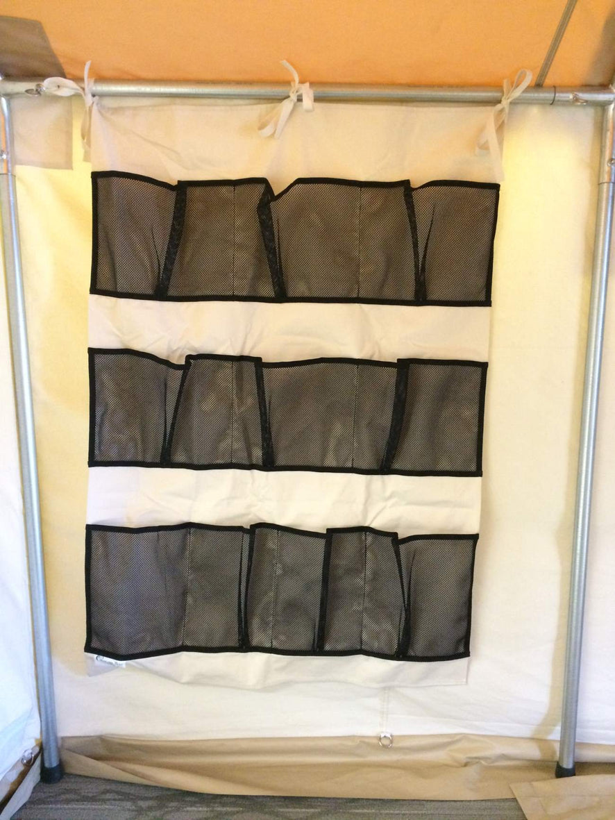 Canvas organizer with nine mesh pockets tied to the frame inside a wall tent.